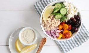A bowl of Chunky Tuna and Cucumber Salad with a side of dressing and lemon wedges