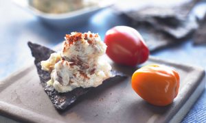 a spoonful of crab dip on top of a blue corn tortilla chip with red and orange bell peppers on the side