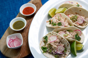 5 plates soft tuna tacos with lime wedges and sauces on the side